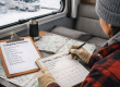 Camper inside an RV planning spring camping trips during winter with a calendar and travel map